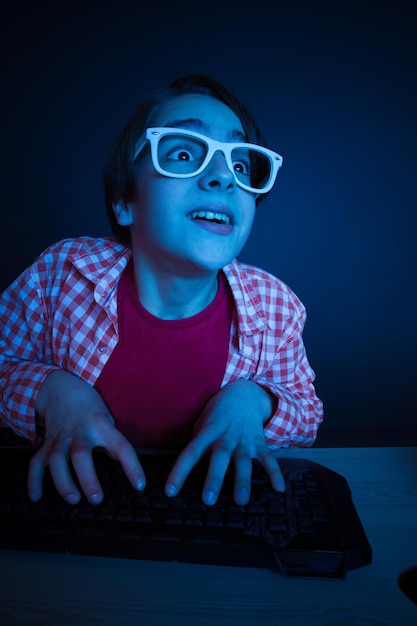 Little boy look to computer display. He like play and win video games. In blue light of display emotional kid play computer games online.