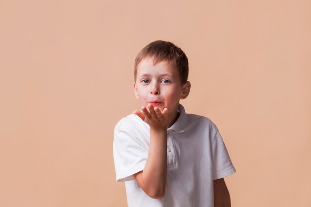 Little boy looking at the camera blowing a kiss with hand on air