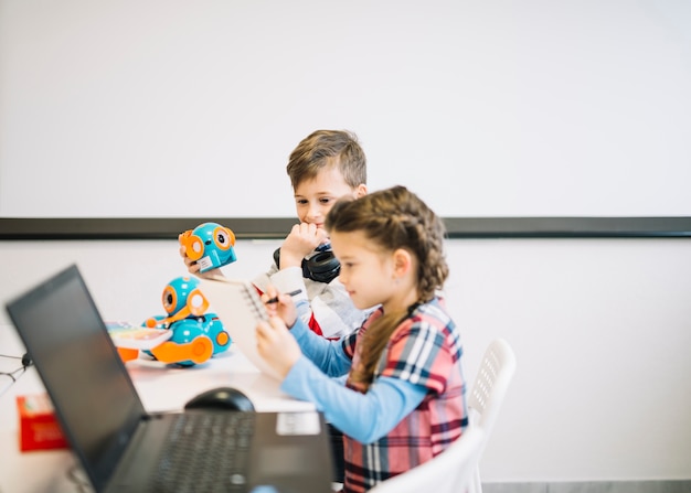 Little boy looking at girl drawing on notebook with pen in the classroom