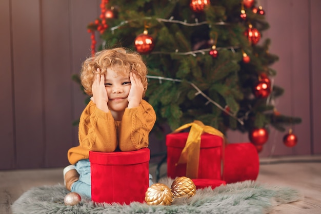 Little boy near christmas tree in a brown sweater