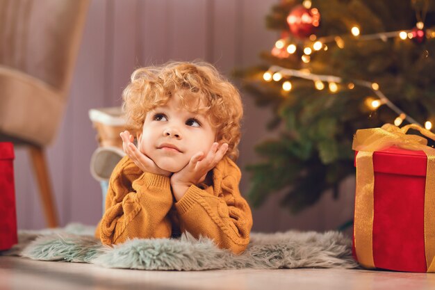 Little boy near christmas tree in a brown sweater