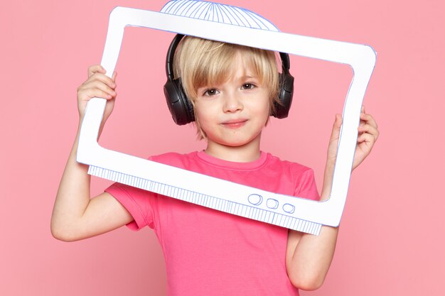 Little boy in pink t-shirt and black headphones listening to music with paper screen