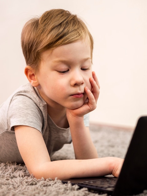 Foto gratuita ragazzino che gioca sul pavimento con il suo computer portatile