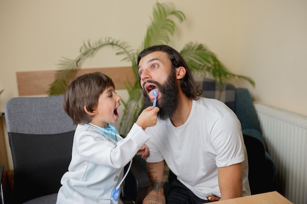 Free photo little boy playing pretends like doctor examining a man in comfortabe medical office