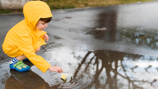 Маленький мальчик играет в воде с бумажный кораблик
