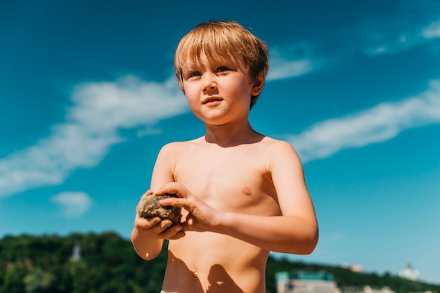 Маленький мальчик, играя с песком во время летних каникул