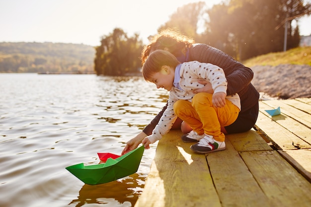 Little boy playing with toy paper ship by the lake