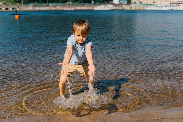 Foto gratuita ragazzino che gioca con acqua sulla riva