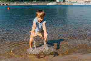 Foto gratuita ragazzino che gioca con acqua sulla riva