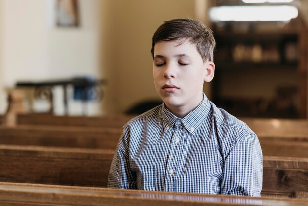 Маленький мальчик молится в церкви с закрытыми глазами