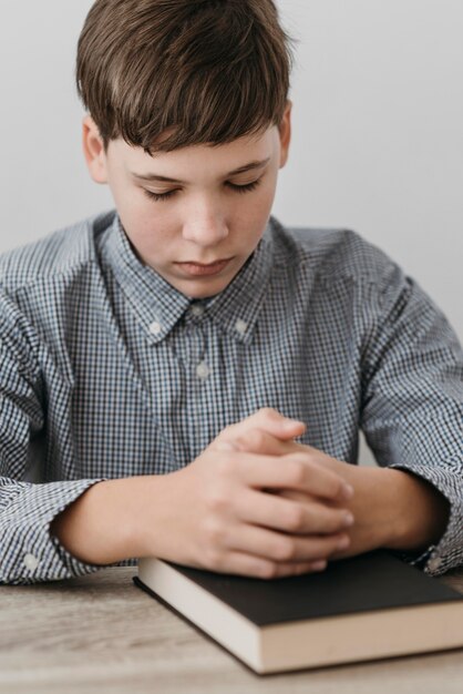 Little boy praying with his hands on a bible