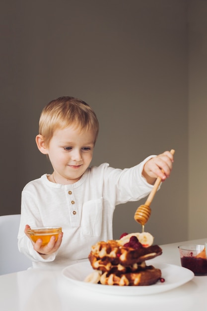 Little boy putting honey on waffle