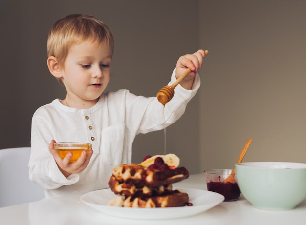 Little boy putting honey on waffle