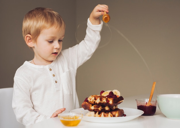 Little boy putting honey on waffle