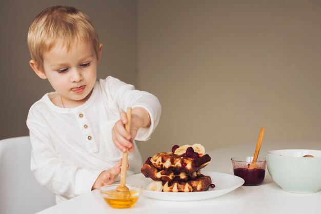 Little boy putting honey on waffle