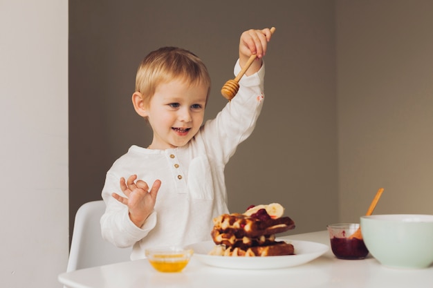 Little boy putting honey on waffle