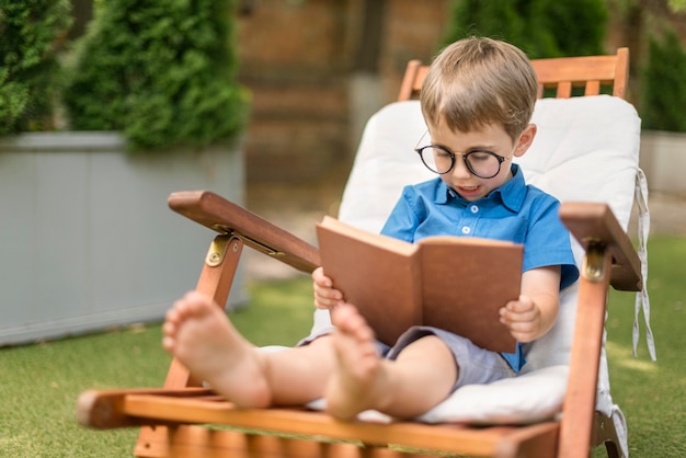 Free photo little boy reading while sitting outside