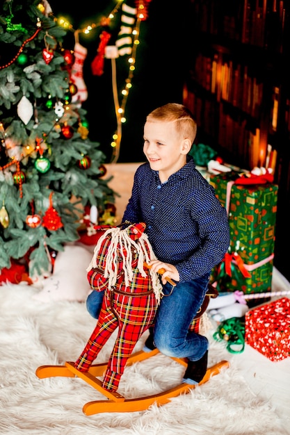 小さな男の子は、クリスマスツリーの前に赤い馬に座っている