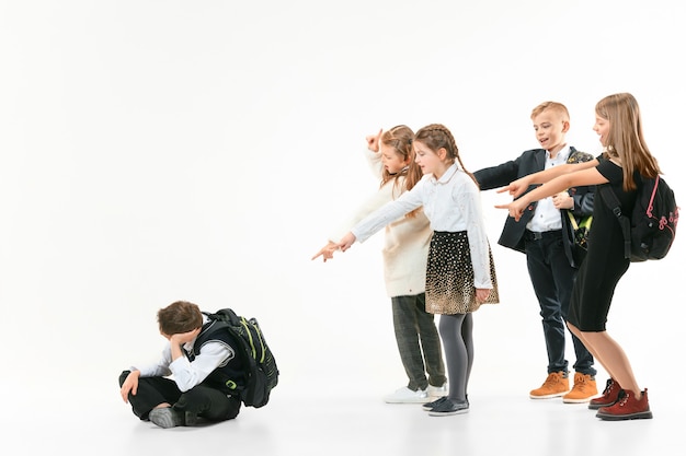 Little boy sitting alone on floor and suffering an act of bullying while children mocking