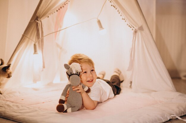 Little boy sitting in cozy tent with lights at home on Christmas