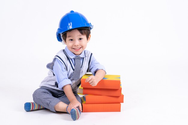 Little boy sitting near stack book on white