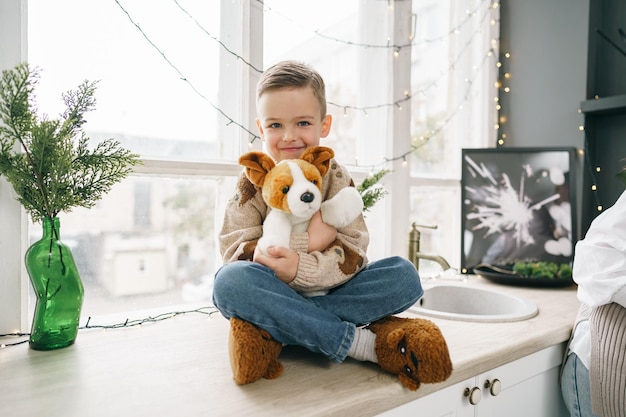 Little boy sitting on windowsill with soft dog toy