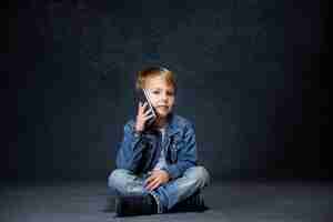 Free photo little boy sitting with smartphone in studio