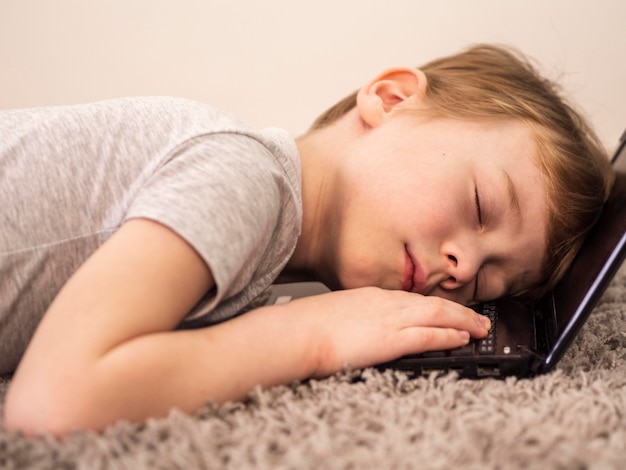 Free photo little boy sleeping on the keyboard of his laptop