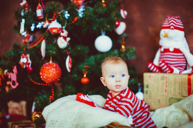 Little boy in stripped pyjamas sits before a Christmas tree 