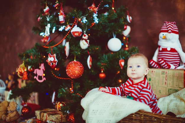 Little boy in stripped pyjamas sits before a Christmas tree 