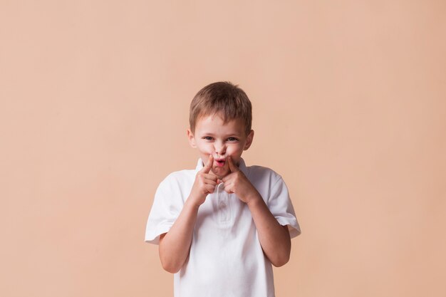 Little boy teasing and looking at camera standing near beige background