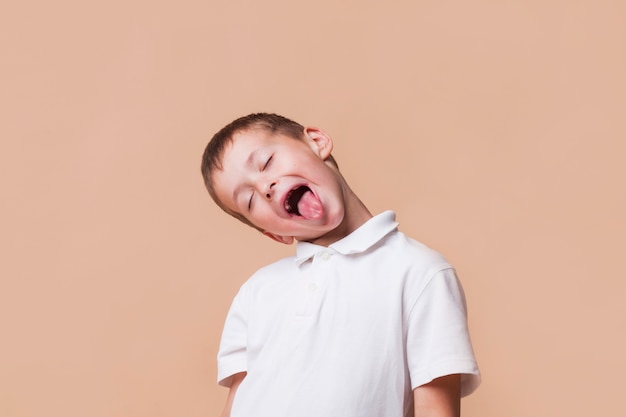Little boy teasing with closed eye on beige background