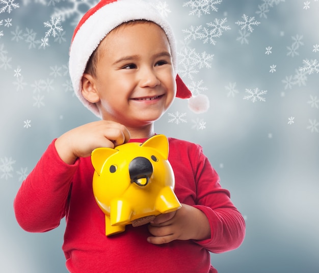 Little boy using his piggybank with snowflakes background