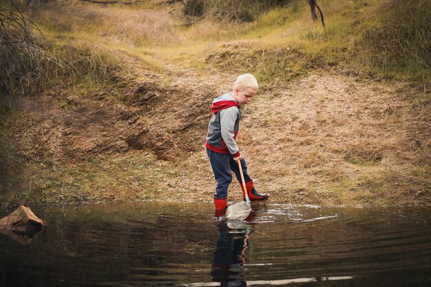 Little boy wearing winter clothing using a net to catch tadpoles