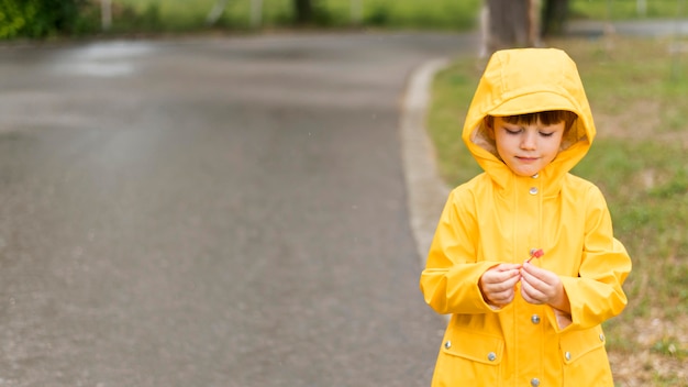 Ragazzino che porta il cappotto di pioggia giallo con lo spazio della copia