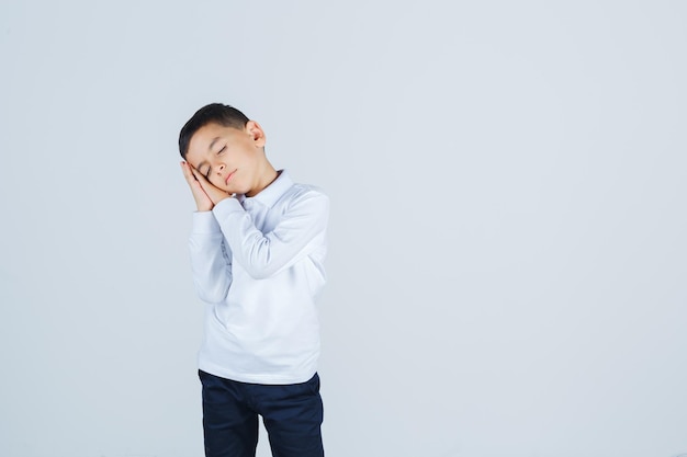 Little boy in white shirt, pants leaning on palms as pillow and looking sleepy , front view.