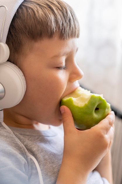 ヘッドフォン食用リンゴの小さな男の子