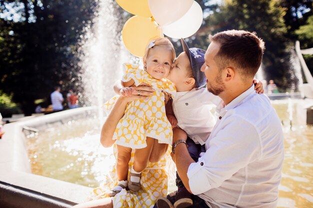 Little brother kisses his little sister standing on father's knees 