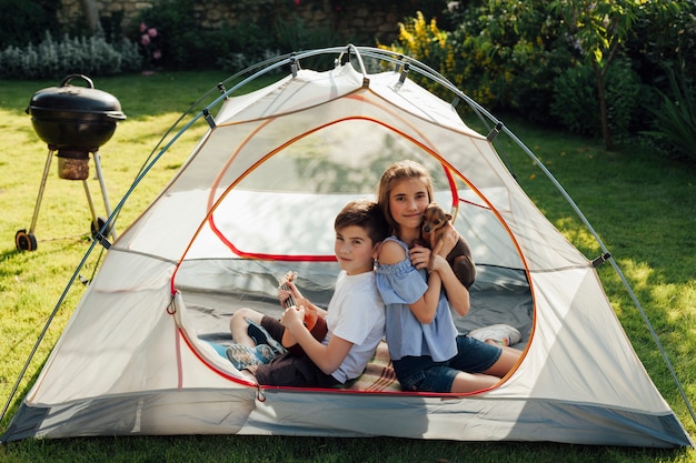 Маленький брат и сестра наслаждаются пикником, сидя в палатке