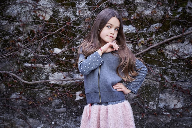 Little brunette girl in a skirt and hoodie on natural grey background.