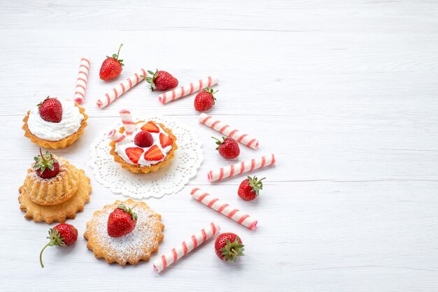 白い机の上にクリームとスライスしたイチゴのキャンディーと小さなケーキ、フルーツケーキベリー甘い砂糖