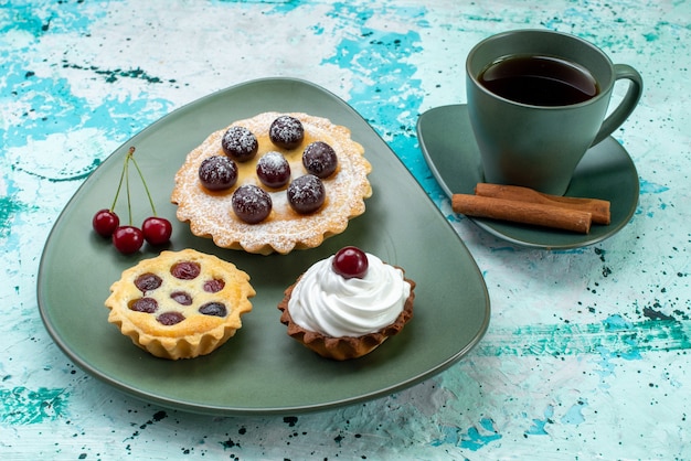 緑のプレートの中に果物が入った小さなケーキと、青のお茶とシナモン、お茶の甘いケーキ焼きパイ