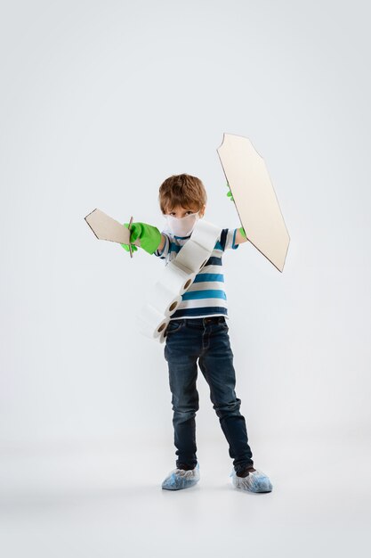 Little caucasian boy as a warrior in fight with coronavirus pandemic, with a shield, a spear and a toilet paper bandoleer, attacking