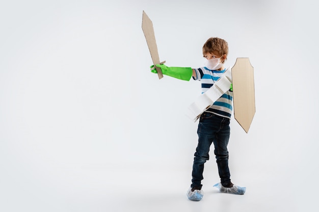 Little caucasian boy as a warrior in fight with coronavirus pandemic, with a shield, a spear and a toilet paper bandoleer, attacking