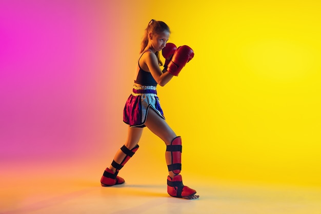 Free photo little caucasian female kick boxer training on gradient background in neon light, active and expressive