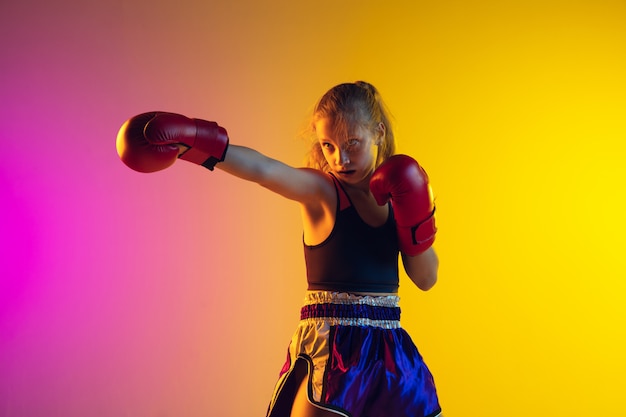 Little caucasian female kick boxer training on gradient background in neon light, active and expressive