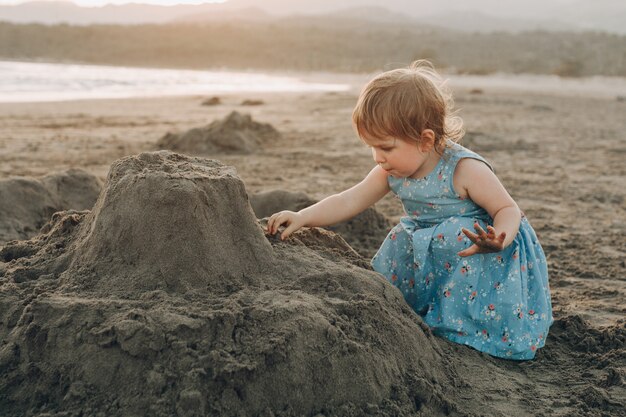 Little caucasian girl have fun digging in the sand at ocean beach, building sand castle