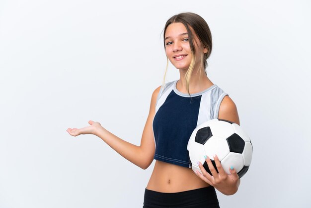 Маленькая кавказская девочка играет в футбол на белом фоне, протягивая руки в сторону, чтобы пригласить прийти