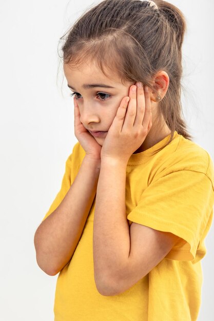 Little caucasian girl thoughtfully holds her head on a white background