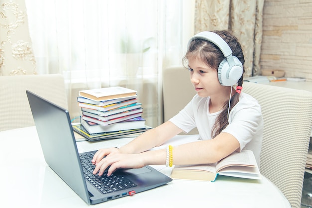 Маленькая кавказская девочка с наушниками смотрит видеоурок на компьютере. онлайн-обучение на компьютере, концепция домашнего обучения.